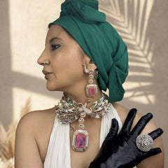 Woman wearing a green headscarf, white dress, black gloves, and jewelry with pink stones.