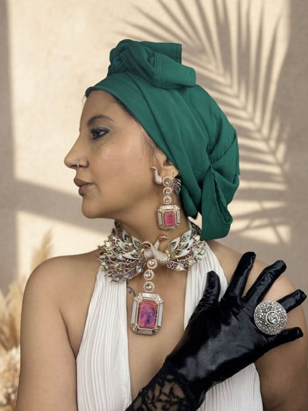 Woman wearing a green headscarf, white dress, black gloves, and jewelry with pink stones.